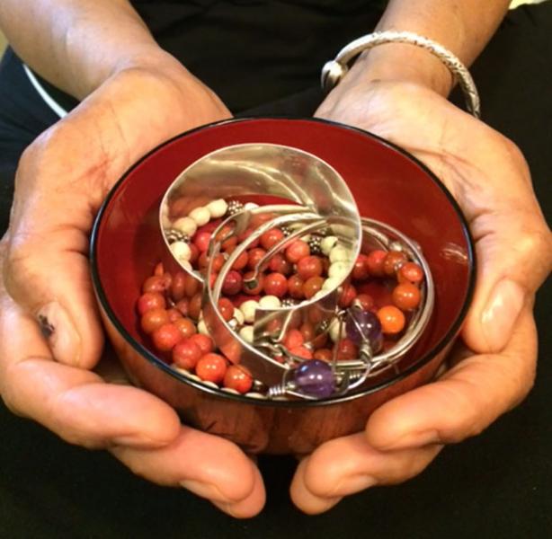 two hands holding a bowl with beads and bangles in it