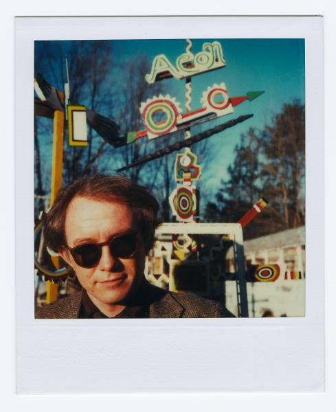 Photo of Tom Patterson wearing sunglasses in front of a whirligig sculpture