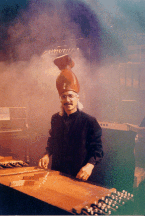 Drummond on the set for Daphne of the Dunes by Harry Partch, playing a harmonic canon, La Mama Experimental Theater, 1994. Hat by Alice Farley. Photo by Jeffrey Starin.